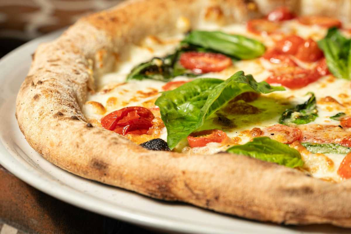Pomodori pelati interi in barattolo di vetro accanto a una pizza napoletana classica con cornicione dorato e salsa di pomodoro