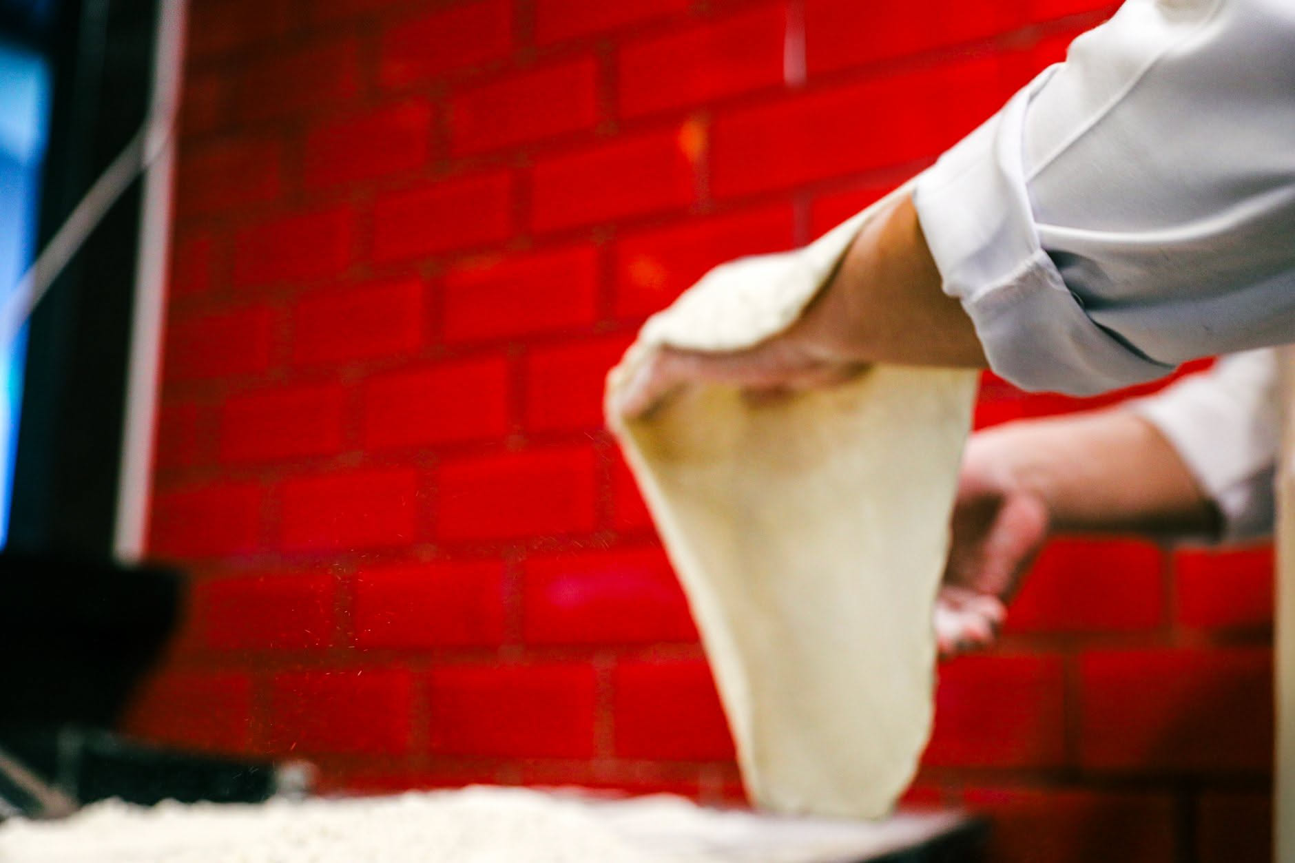 Primo piano di farina bianca di frumento in un ciotola di ceramica accanto a una pizza appena sfornata dal forno a legna con cornicione dorato e leggermente bruciato ai bordi