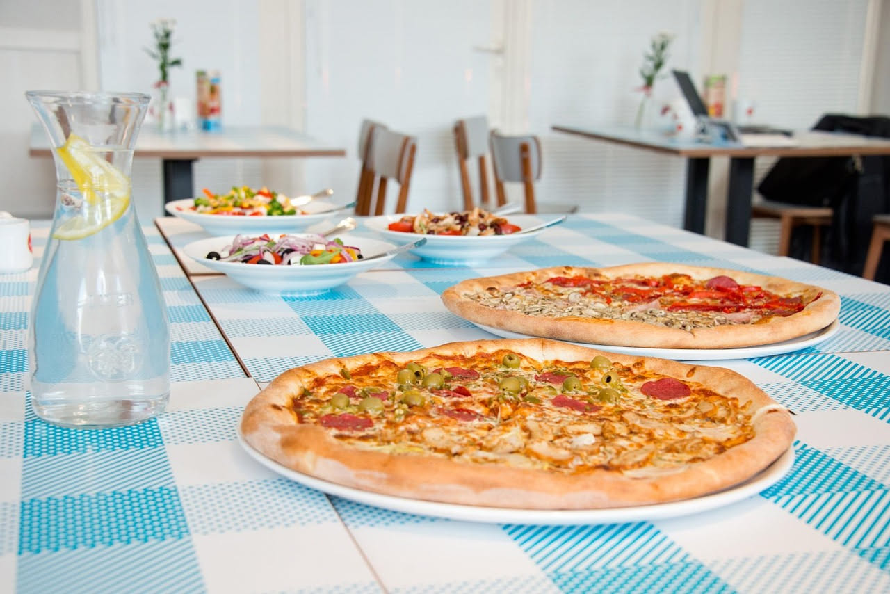Banco pizzeria con piano in marmo bianco, cassettoni refrigerati in acciaio inox sottostanti, pala di legno poggiata sul ripiano, e contenitori trasparenti con ingredienti