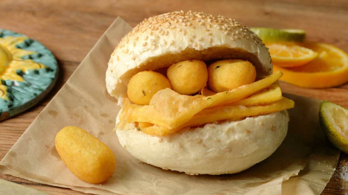 Pizza fritta dorata e croccante appena tolta dall'olio, spezzata a metà per mostrare l'interno, con ricotta e ciccioli di maiale sparsi sulla carta bianca