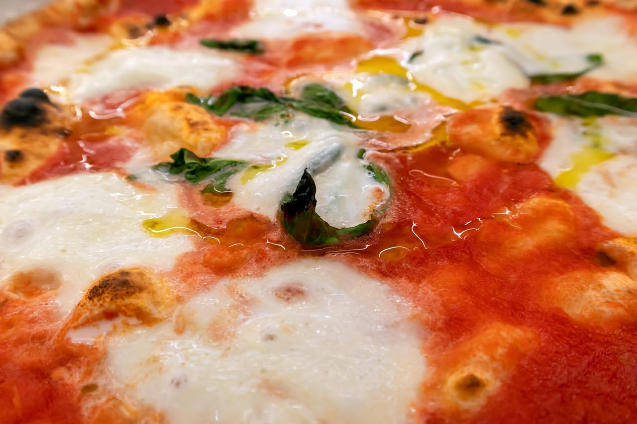 Primo piano di una pizza napoletana appena uscita dal forno con cornicione gonfio, dorato e lievemente bruciato ai bordi, su sfondo scuro