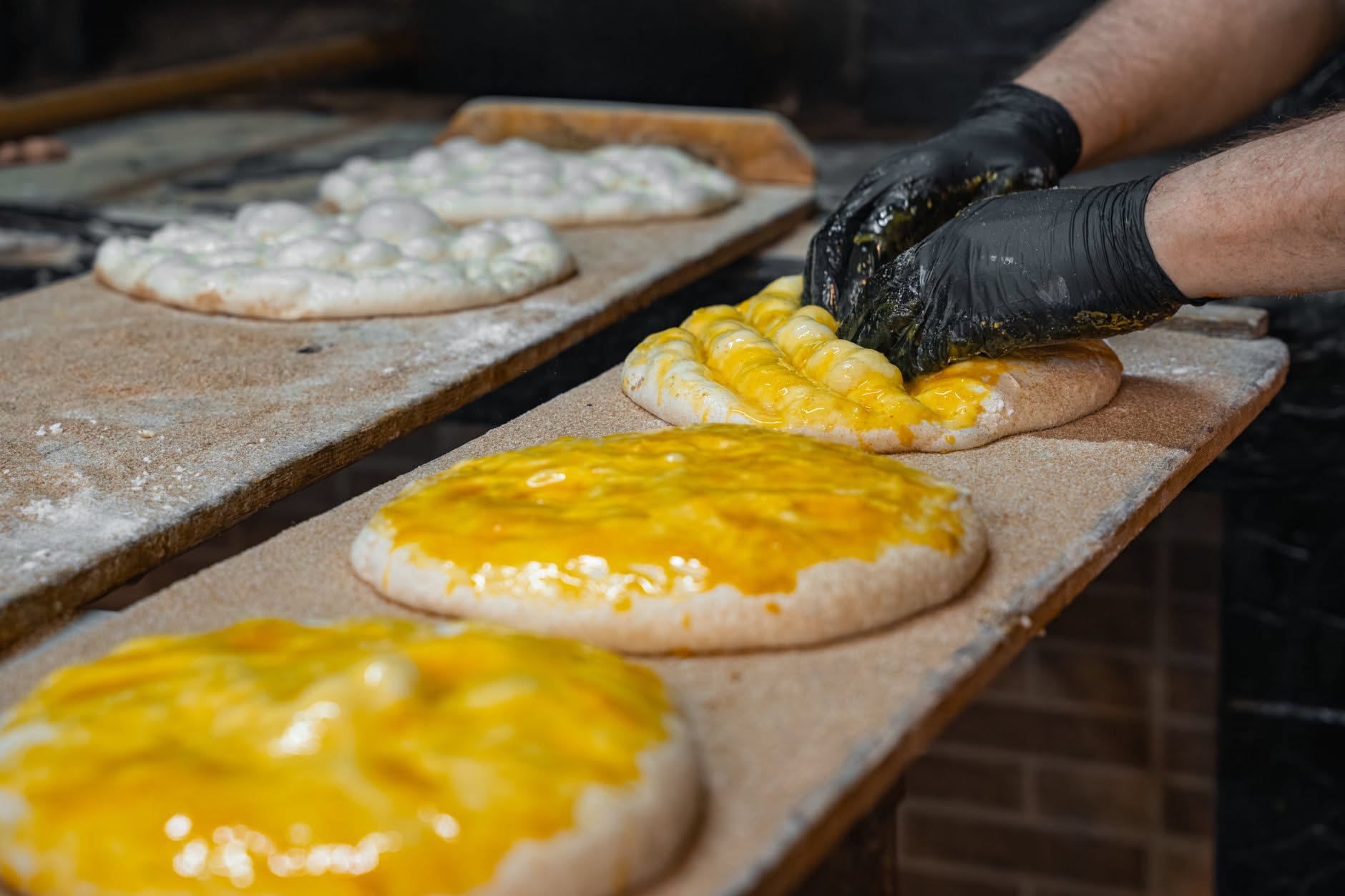 Mani di un pizzaiolo che stendono un impasto di pizza romana su una teglia oliata, visto dall'alto, con spessore sottile e uniforme