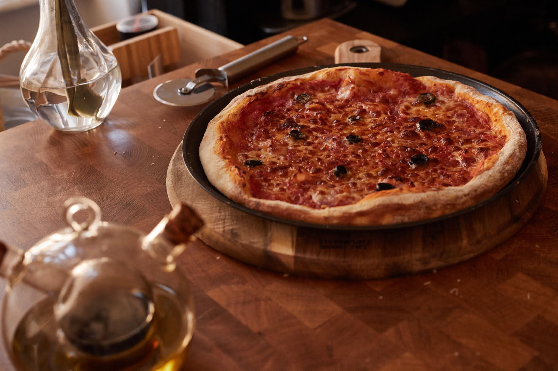 Mani di un pizzaiolo che stendono con le dita un impasto di pizza su una teglia rettangolare, vista dall'alto, impasto giallo pallido e uniforme