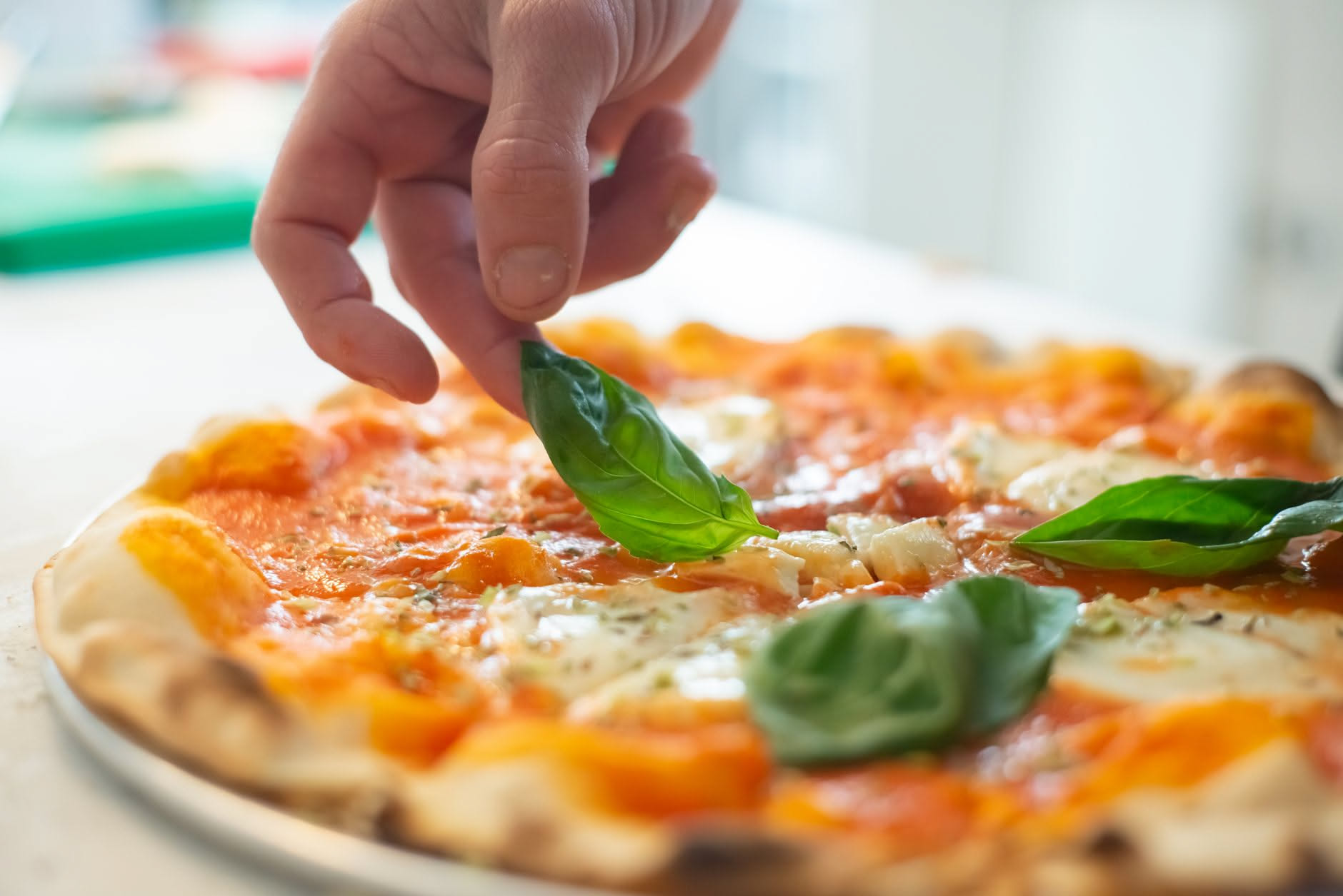 Mani di un pizzaiolo che stendono un disco di impasto di pizza napoletana su un piano di marmo, con le dita aperte e il movimento che va dal centro verso l'esterno