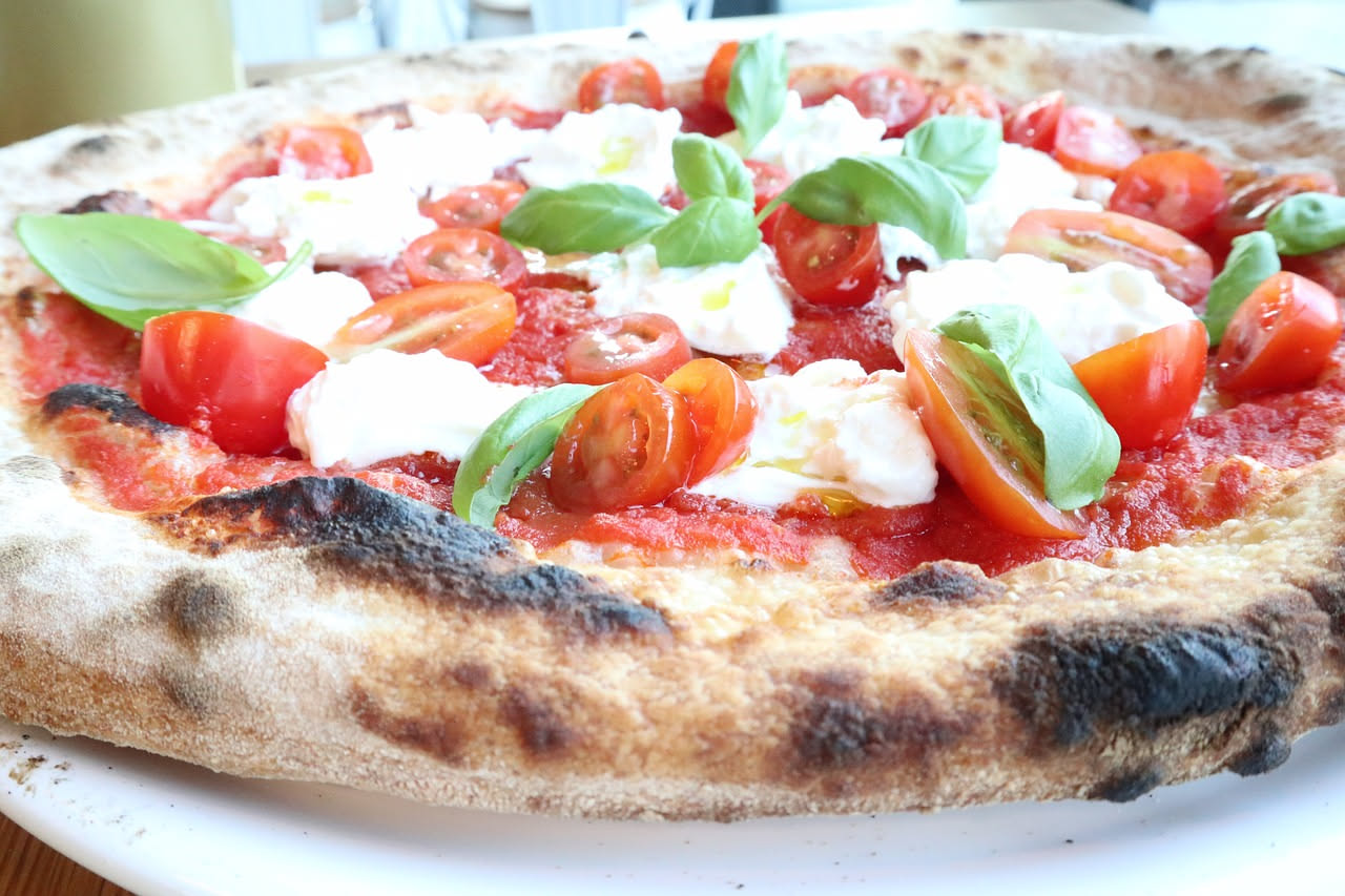 Pizzaiolo napoletano di fronte a forno a legna rosso con pizza appena infornata, cornicione gonfio e dorato, mani che girano la pala di legno