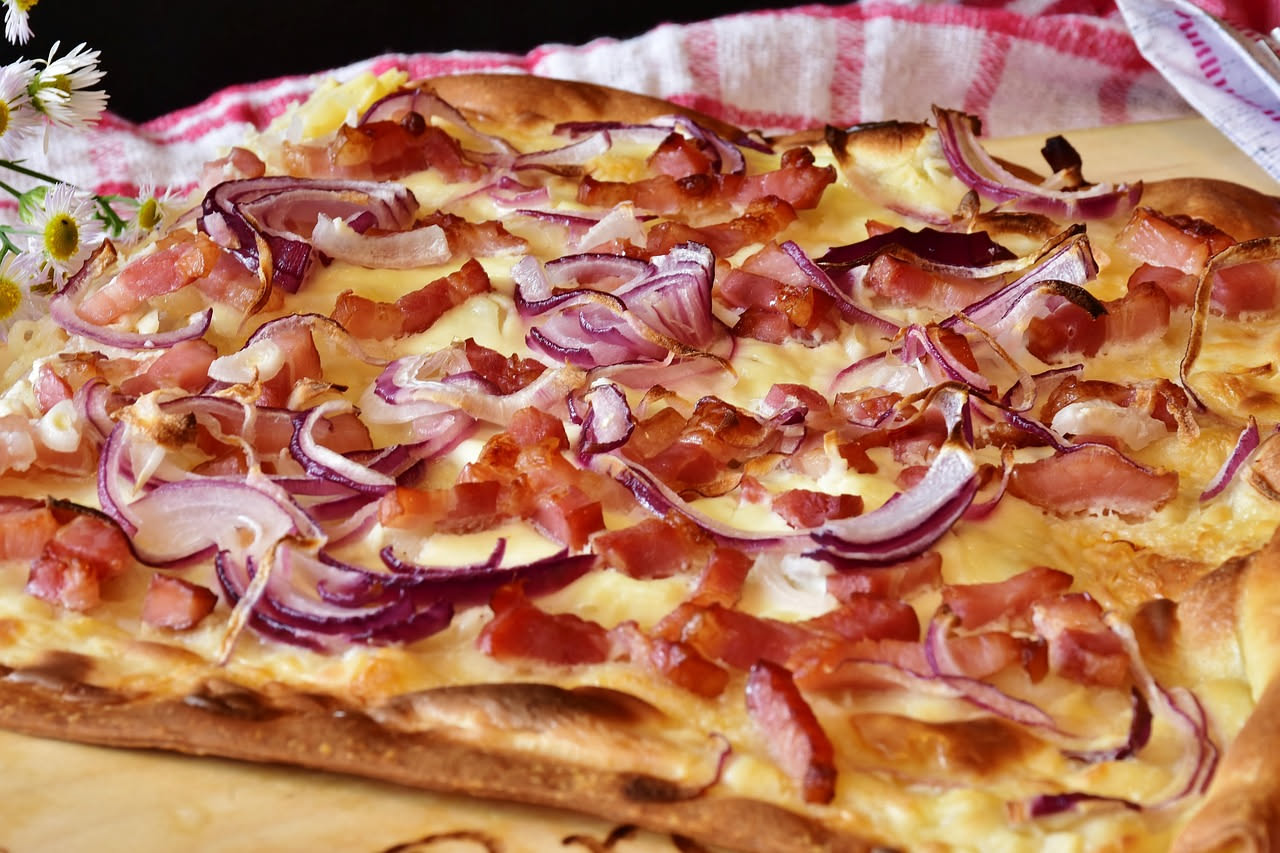 Pizza romana tagliata a quadrati su teglia di metallo, con crosta dorata e croccante, vapore che sale dalla superficie, ingredienti freschi visibili
