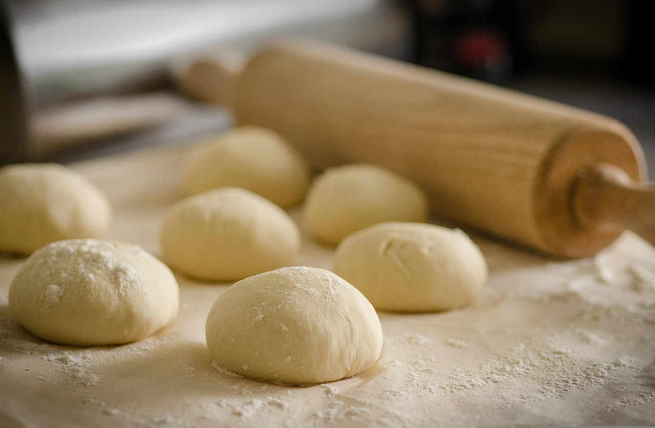 Pizzaiolo con le mani infarinate che stende un impasto su una superficie di marmo bianco, con un forno a legna sullo sfondo che irradia calore rosso arancio