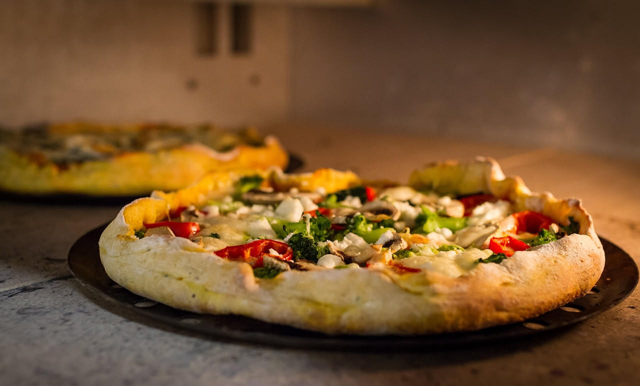 Mani di pizzaiolo che allargano un impasto di pizza bianco su un piano di lavoro infarinato, mostrando il passaggio da una pallina compatta a un disco sottile