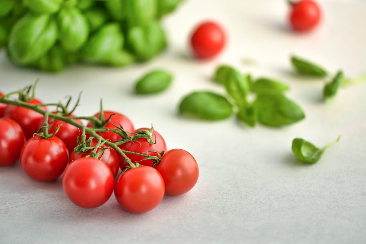 Tre varietà di pomodorini a confronto: datterini rossi allungati, piennoli tondi con picciolo, pomodorini ciliegini, disposti su tavolo di legno con foglie di basilico