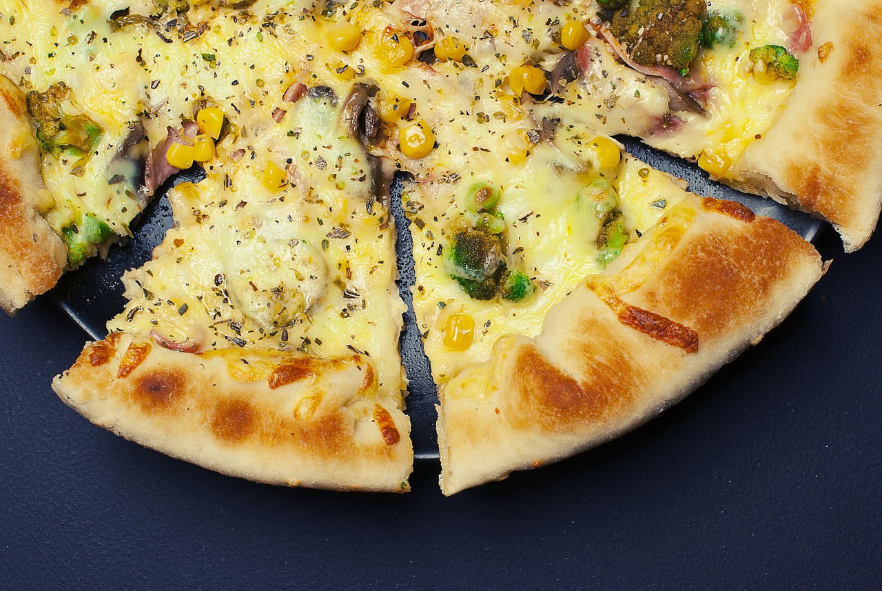 Sezione trasversale di una pizza deep dish marrone chiaro in una teglia rettangolare, a fianco sezione di stuffed pizza con doppio strato di impasto e formaggio visibile