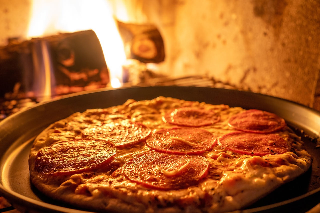 Interno di un forno a legna tradizionale con fiamme arancioni sulla base in mattoni refrattari e volta arrotondata