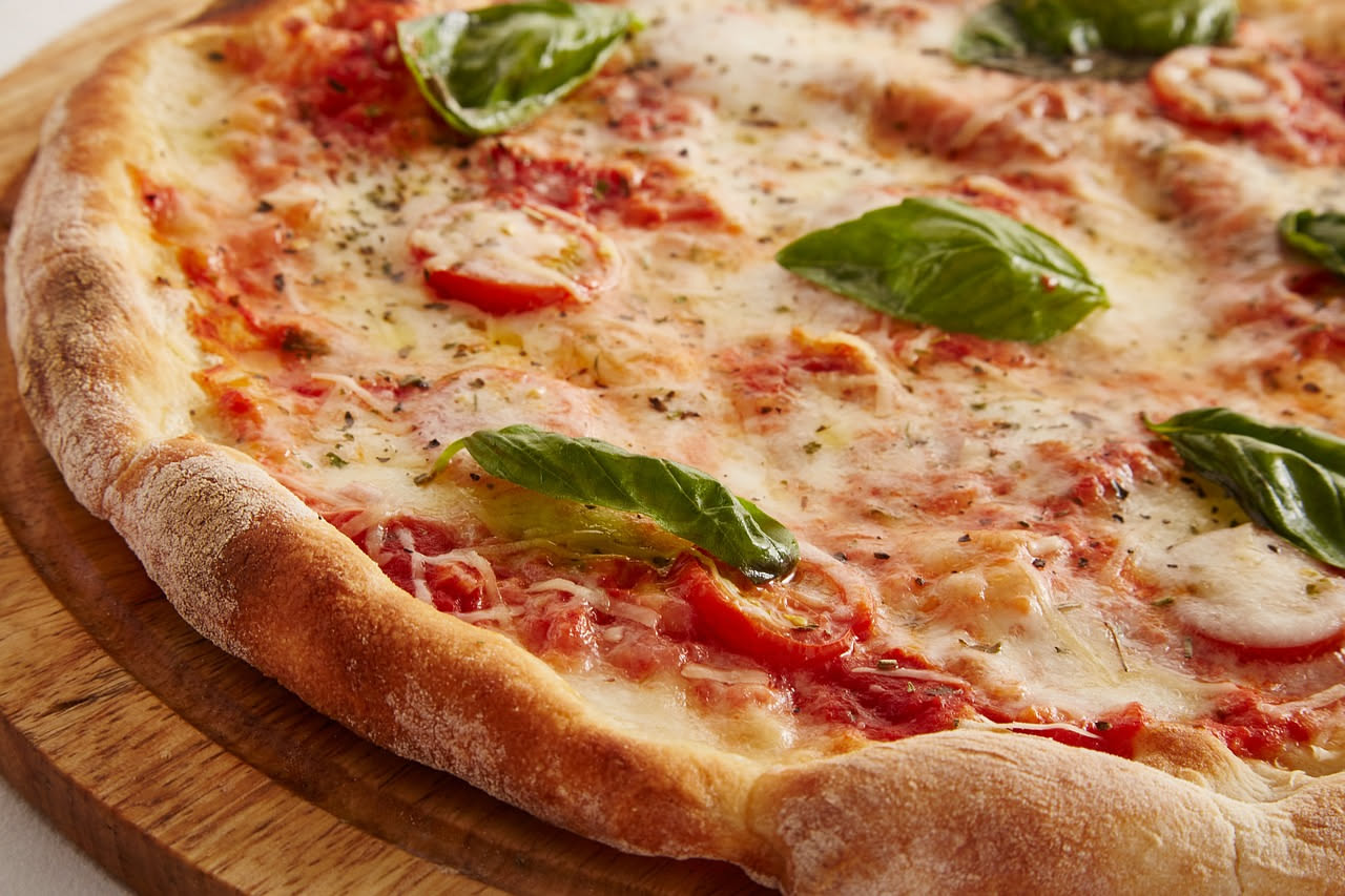Pizza margherita appena sfornata con basilico fresco verde applicato sopra ancora fumante, mozzarella bianca e pomodoro rosso