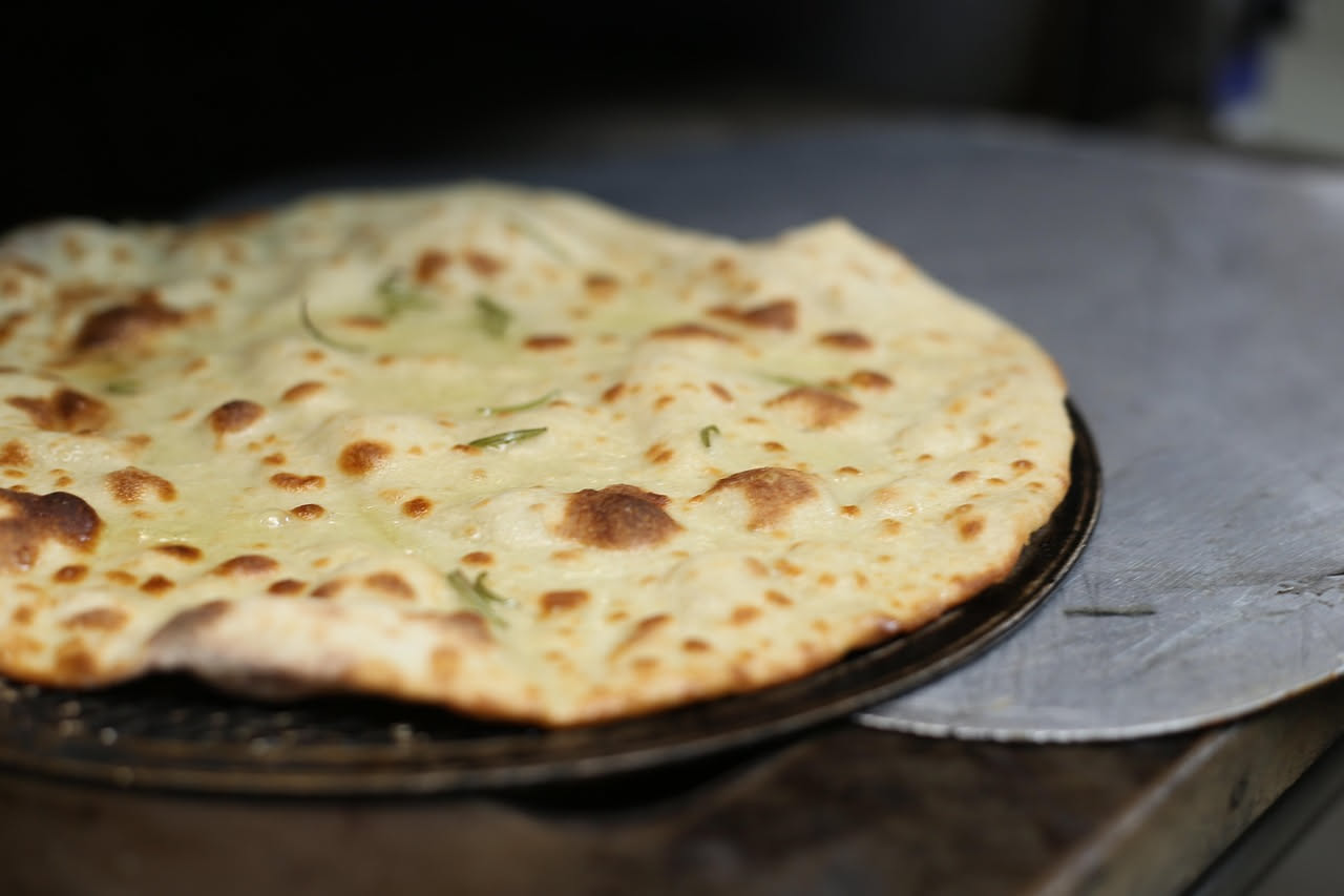Dettaglio di una pizza napoletana appena sfornata, con cornicione gonfio e dorato, alveoli visibili in sezione trasversale