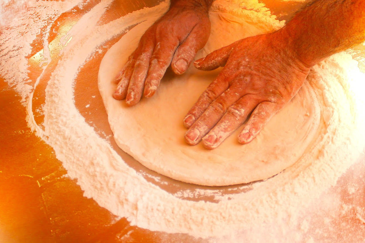 Pasta di lievito madre color beige con bolle visibili in una ciotola di ceramica bianca, accanto a un mestolo di legno e farina bianca su un piano di lavoro in marmo