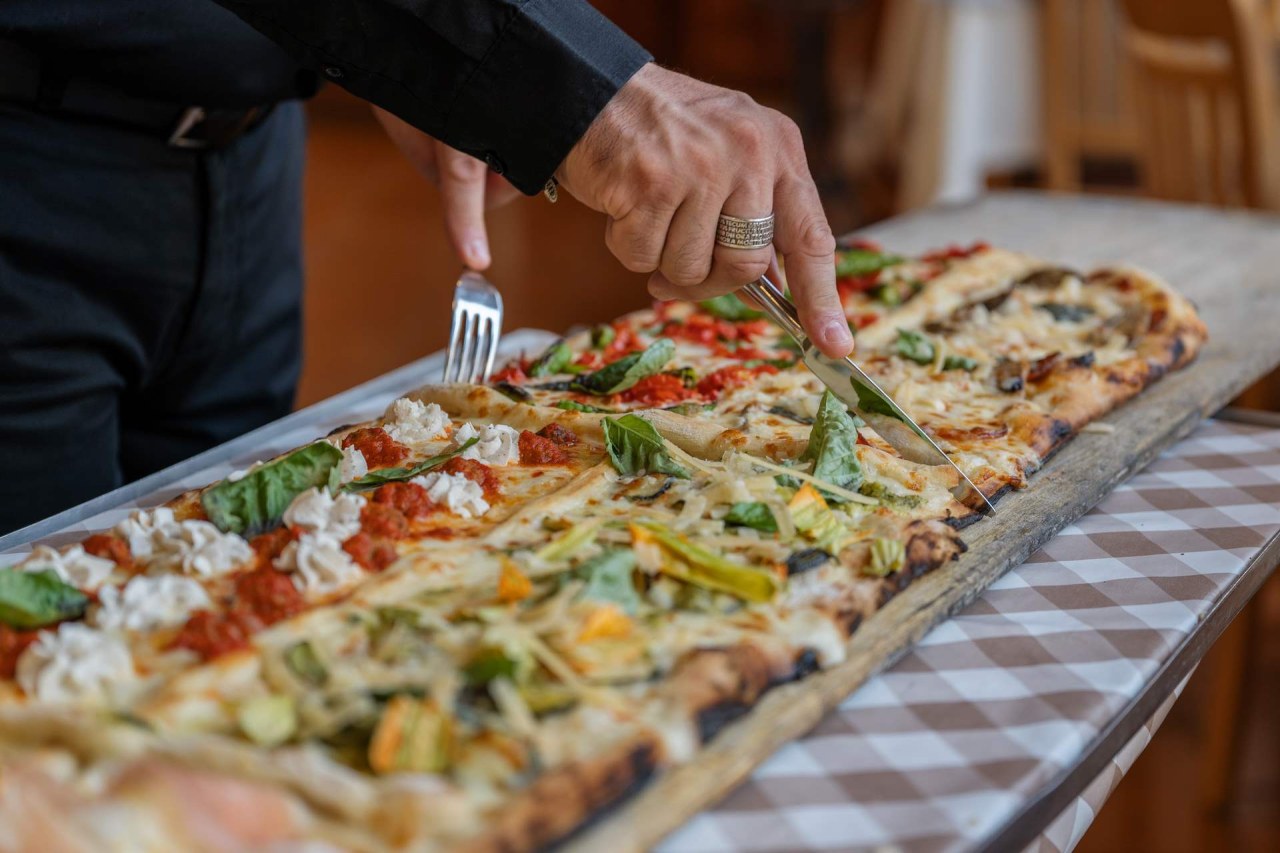 Una lunga tavola di legno con pizza tagliata al metro, incartata in carta bianca, al tramonto con la costiera sorrentina sullo sfondo