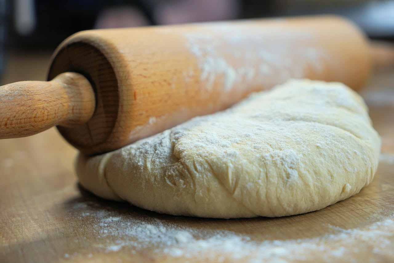 Due impastatrici professionali in acciaio affiancate, una con braccio a spirale e una con forcella, dentro una cucina di pizzeria con farina bianca sul piano di lavoro
