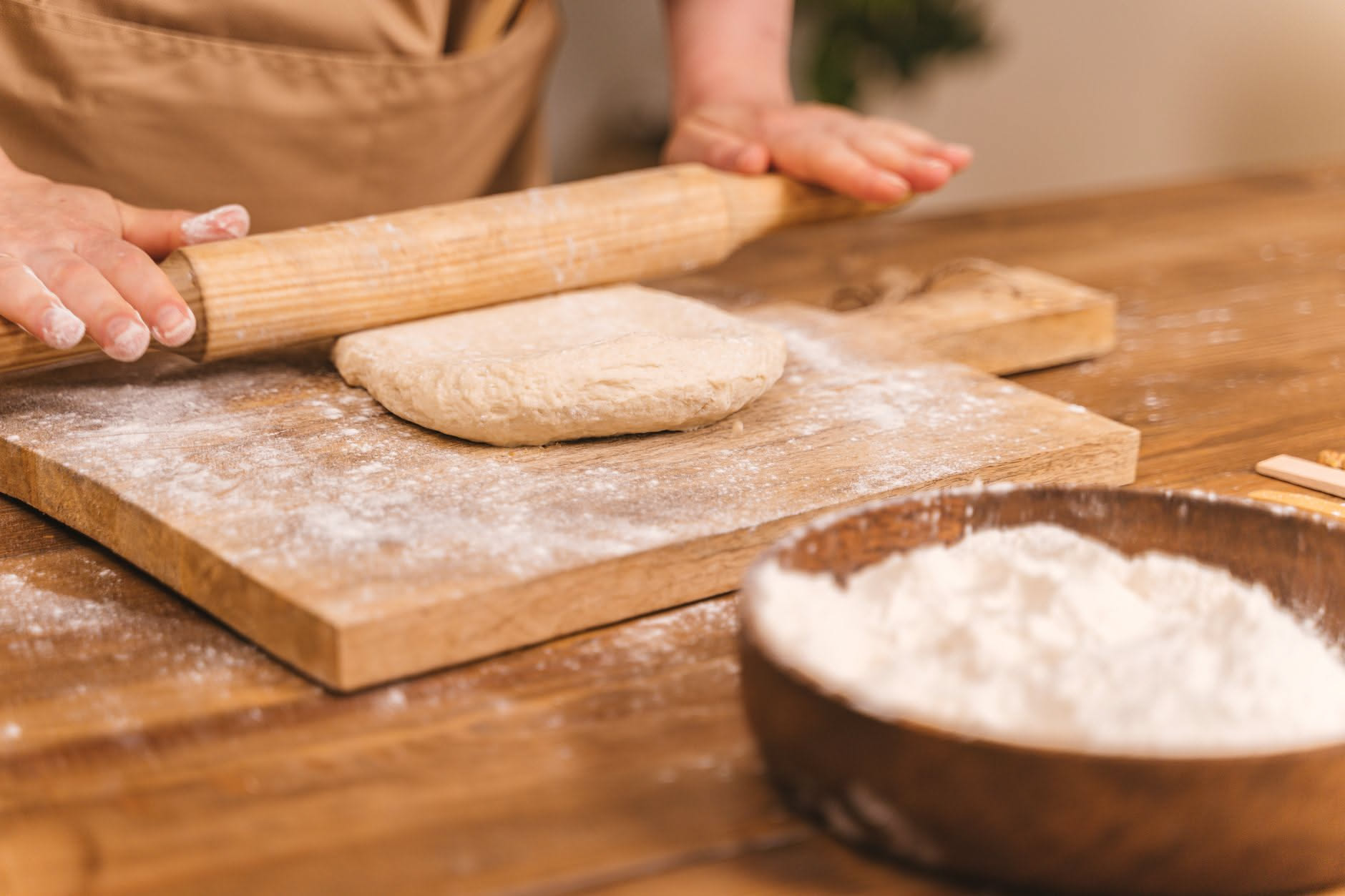 Mani di pizzaiolo che lavorano un impasto leggermente appiccicoso su piano infarinato, con gocce d'acqua visibili sulla superficie e una ciotola con impasto sullo sfondo