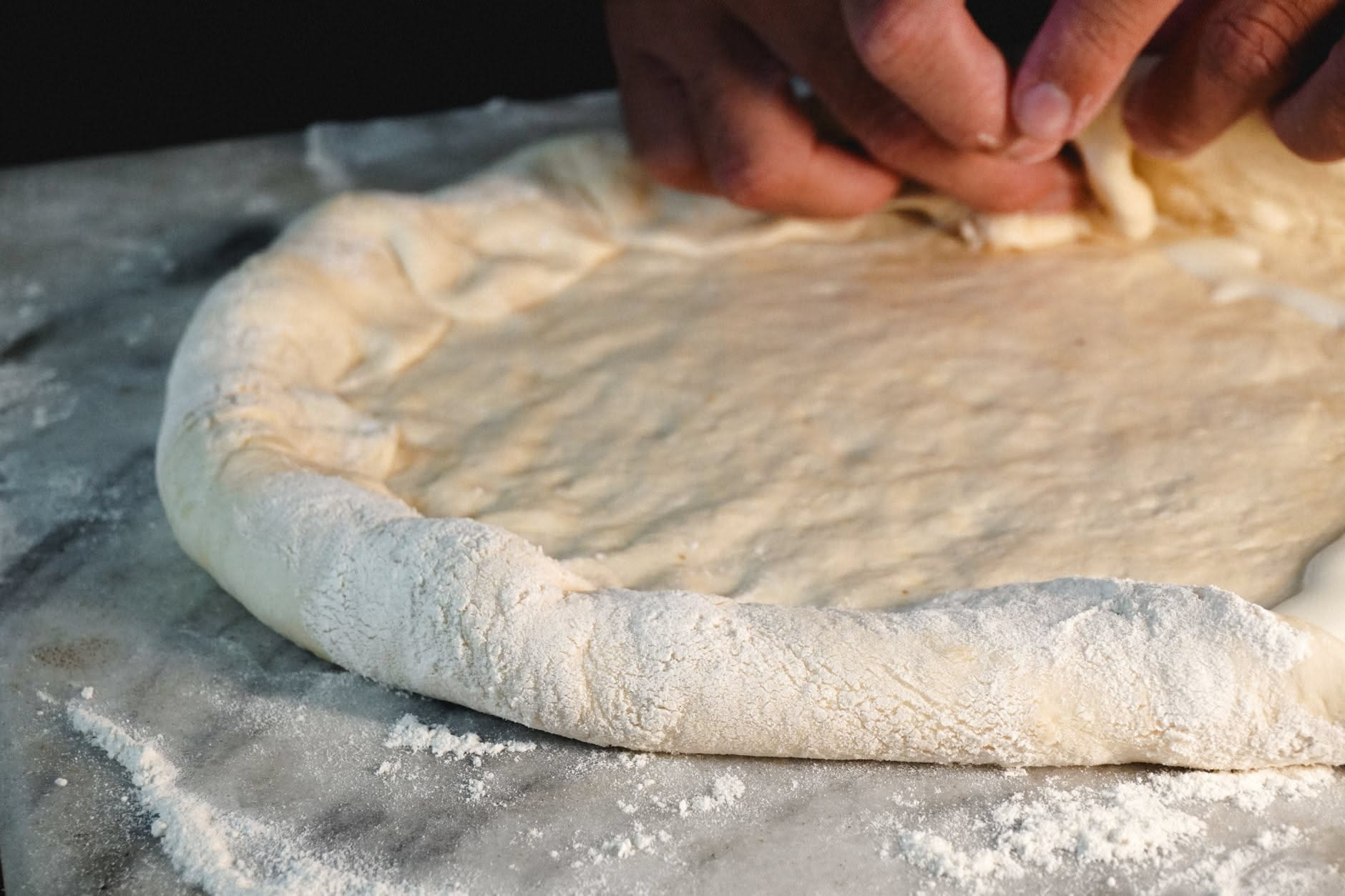 Impasto di pizza in una ciotola, elastico e umido, con una leggera patina di olio; accanto un cronometro e un bicchiere graduato con acqua
