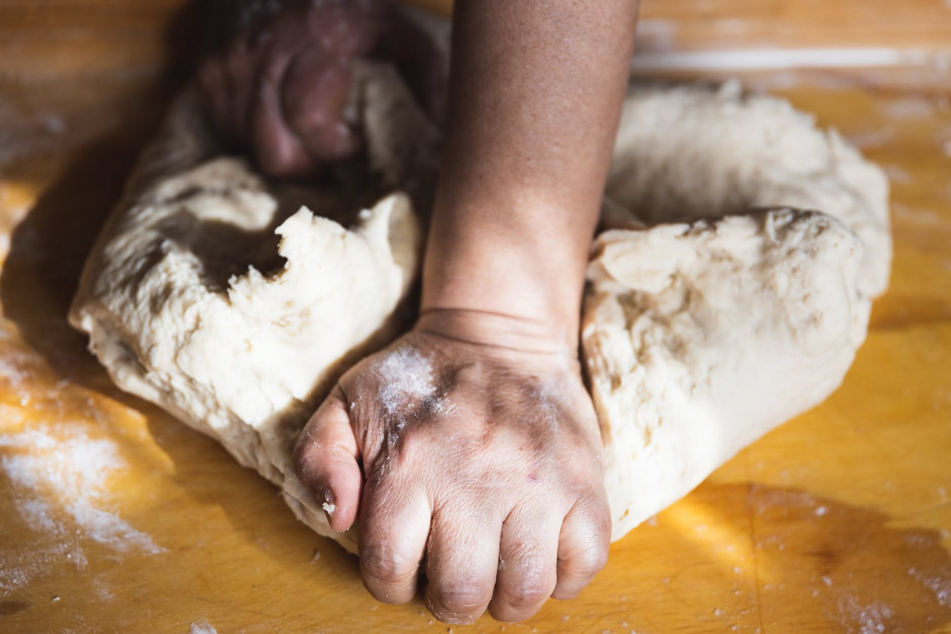Panetto di impasto per pizza che si lacera mentre viene allargato con le mani, mostrando una texture fragile e disomogenea