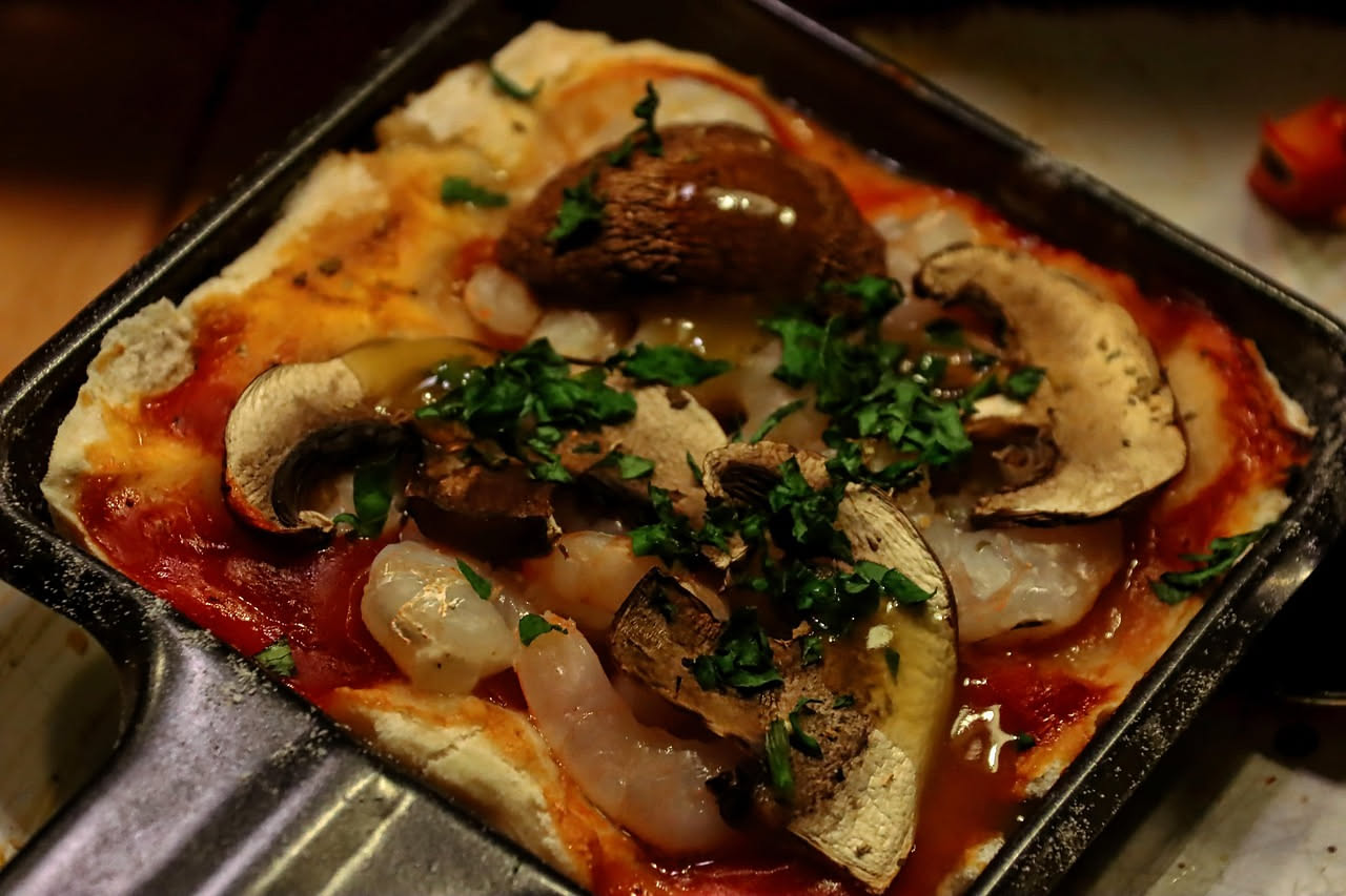 Pizza quadrata Detroit style con formaggio fuso e caramellizzato sui quattro bordi, condimento in centro, cotta in teglia rettangolare, vista dall'alto