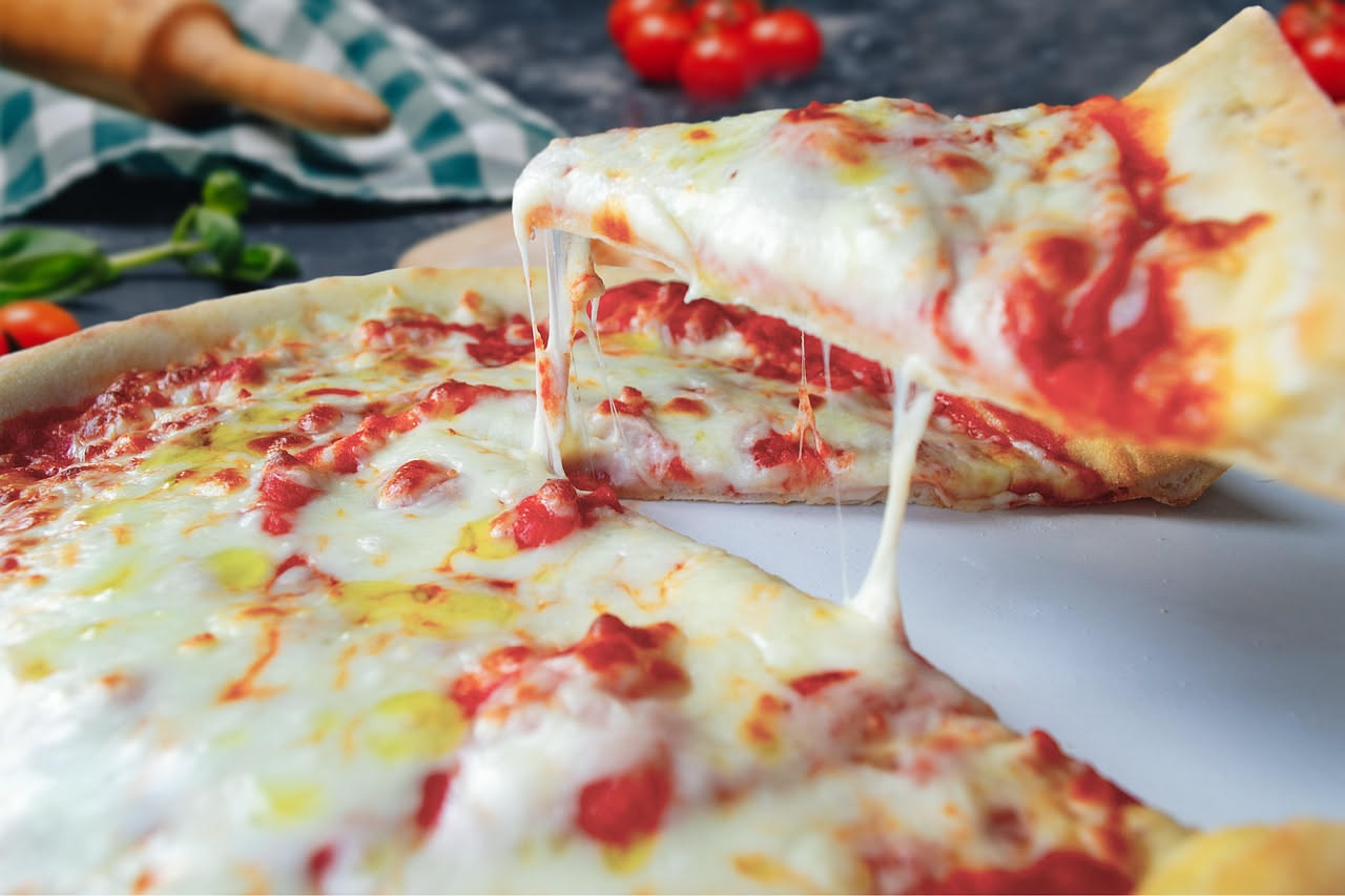 Mani di pizzaiolo che allungano un impasto su una pala di legno davanti a un forno a legna, con il cornicione che si forma naturalmente ai bordi