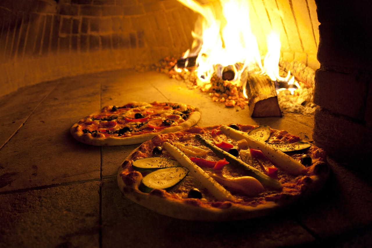 Stufo di rame tondo e piatto con coperchio a cupola, lucidato e riflettente, posato su un tavolo di legno con sullo sfondo un forno a legna