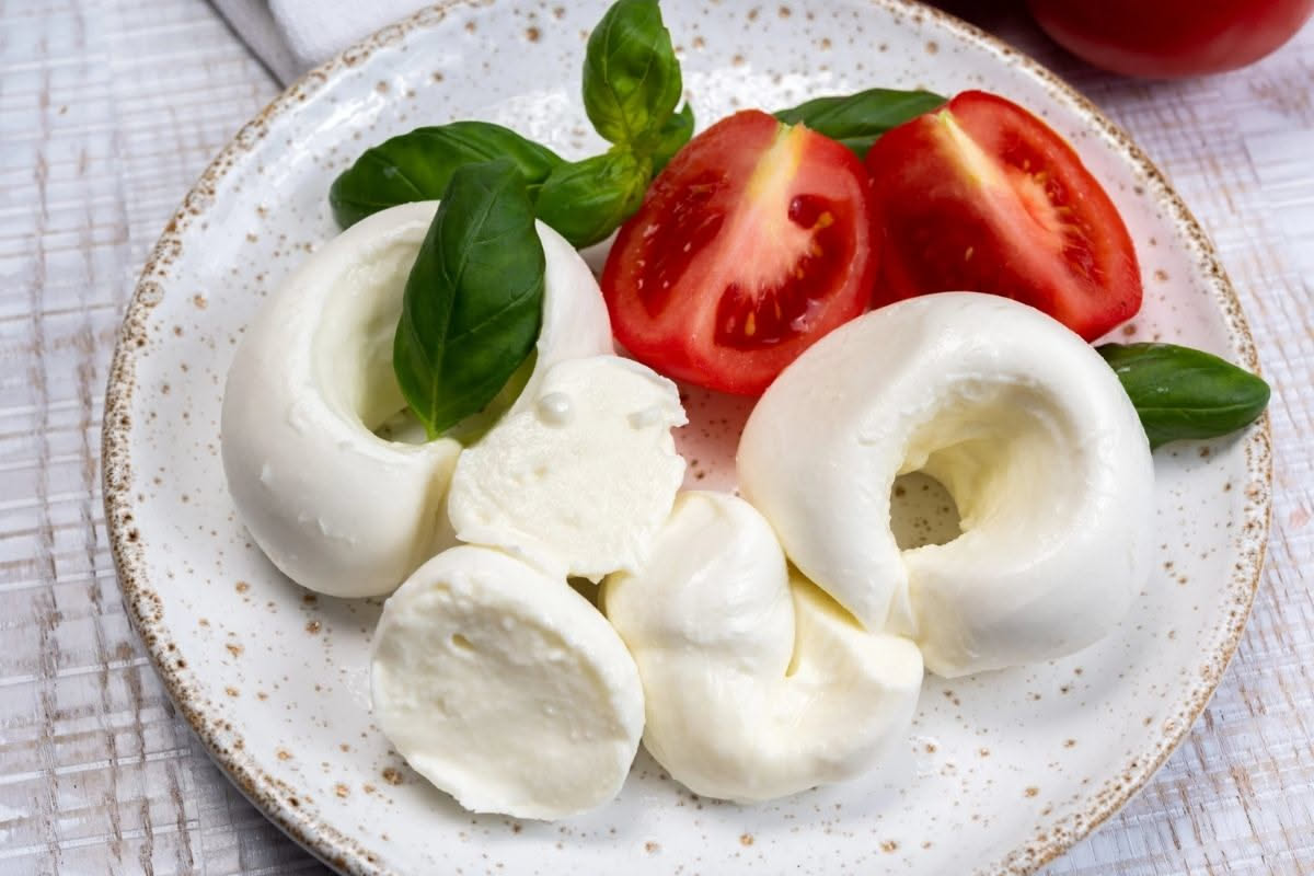 Mozzarella bianca e filante su impasto di pizza, visibile la differenza di umidità e superficie tra formaggio appena filato e quello congelato precedentemente