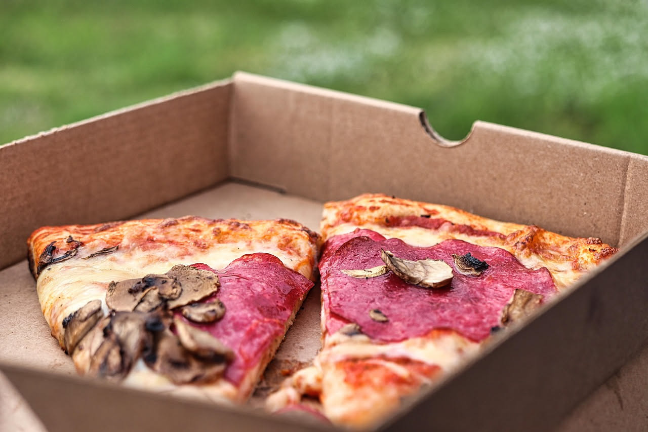 Pizzaiolo in grembiule bianco al bancone di una pizzeria accoglie un cliente per ordinare direttamente, forno a legna sullo sfondo