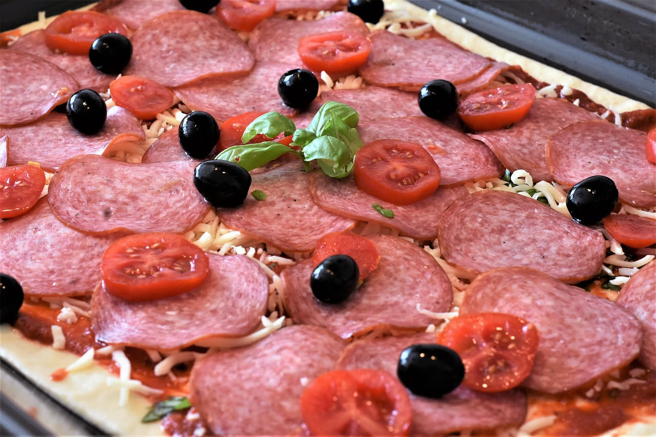 Pizza in teglia durante la seconda cottura in forno a legna, con formaggio fuso e condimenti, croccante ai bordi e soffice al centro