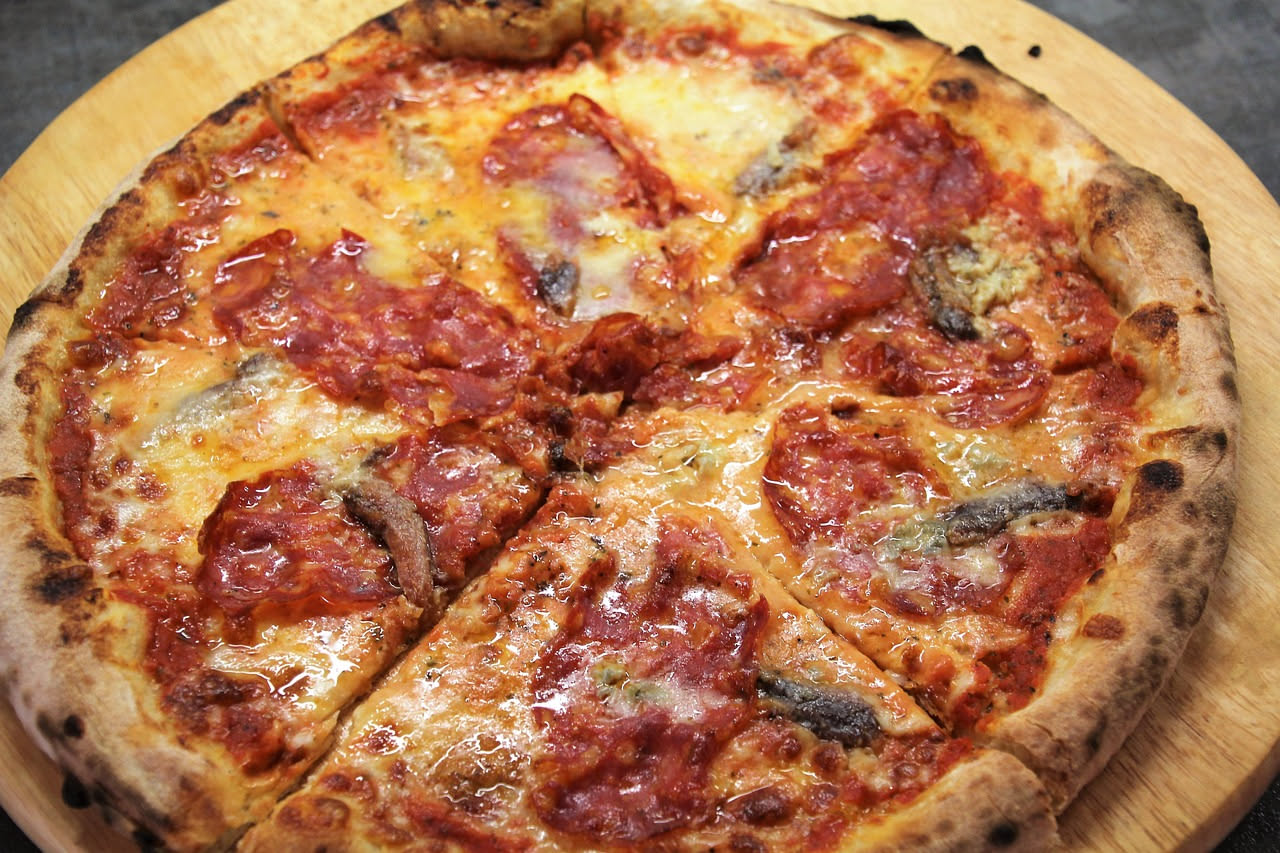 Pizza marinara appena sfornata con cornicione dorato, pomodoro rosso vivo, aglio affettato, origano secco e olio extravergine di oliva lucido su tavolo di legno scuro