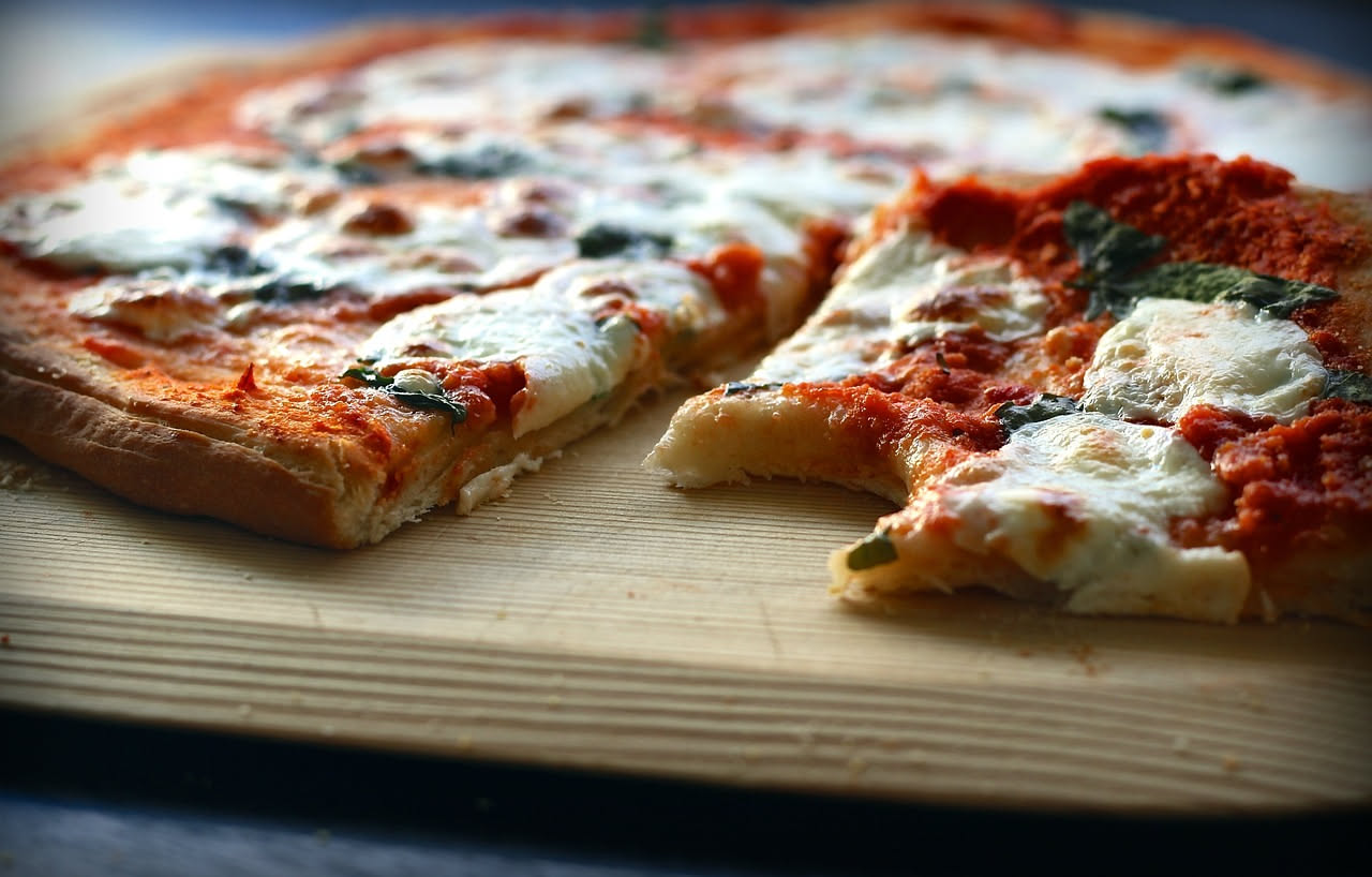 Mani di pizzaiolo che stendono impasto di pizza romana con mattarello di legno su superficie infarinata, spessore sottile e uniforme visibile