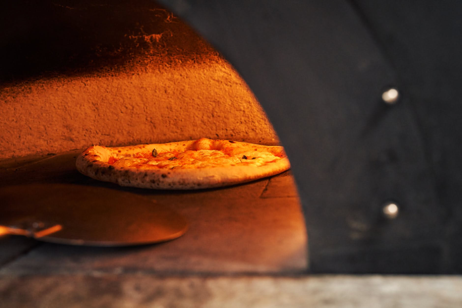 Tre diversi supporti per pizza disposti su un piano di lavoro: una pietra refrattaria beige, una piastra d'acciaio grigia scura e una teglia in metallo rovesciata