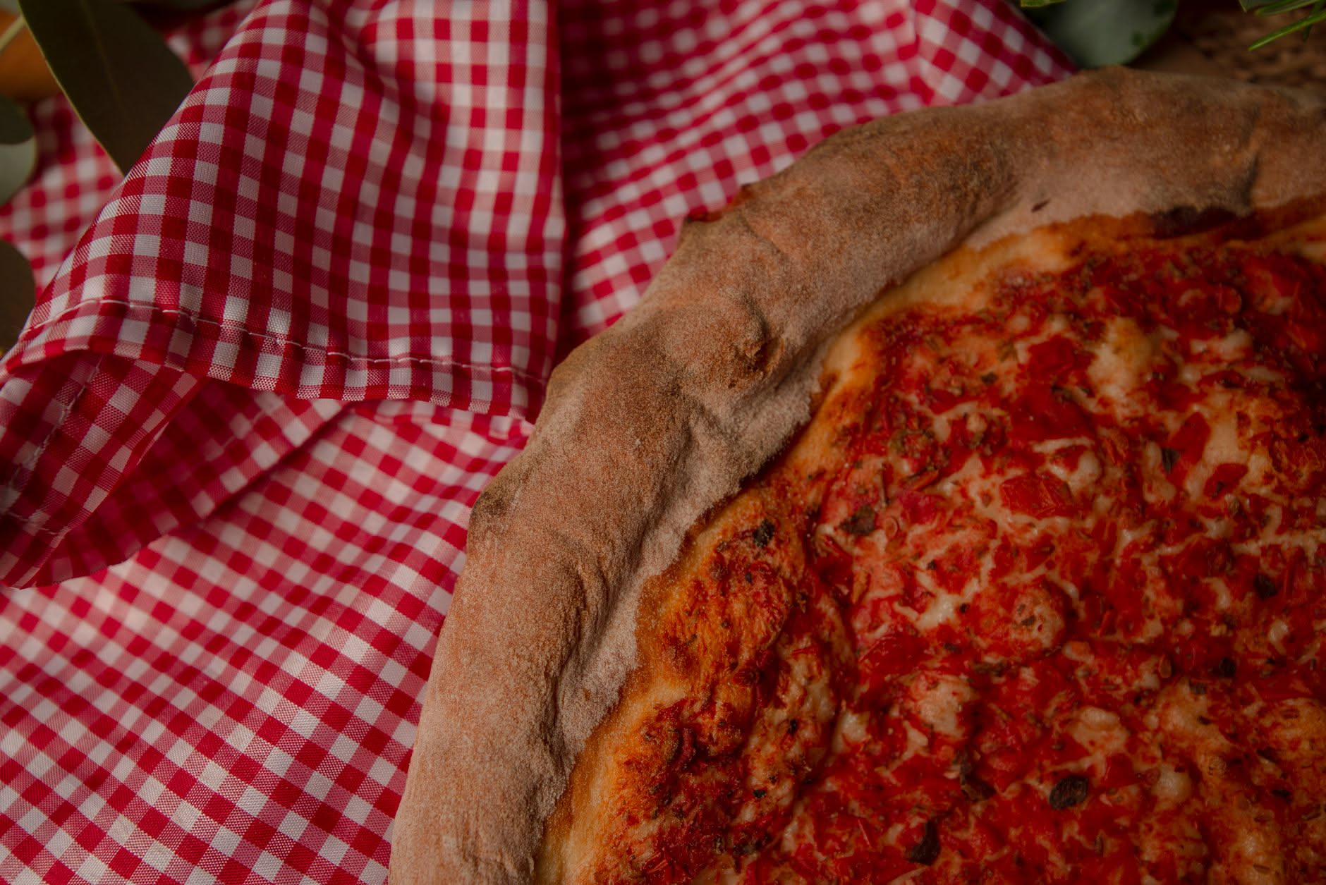 Mani che stendono un disco di impasto su una teglia bianca, con una ciotola di pomodori rossi e un barattolo di olio d'oliva in background