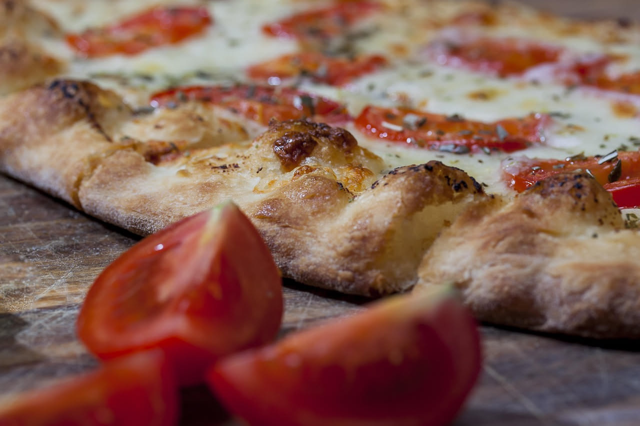 Impasto di pizza in lievitazione dentro una ciotola trasparente, con bolle d'aria visibili, accanto a un termometro che segna 28 gradi