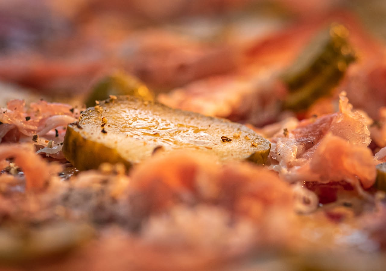 Pizzaiolo versa olio extravergine di oliva da una bottiglia su una pizza appena sfornata, con mozzarella filante e pomodoro fresco visibili