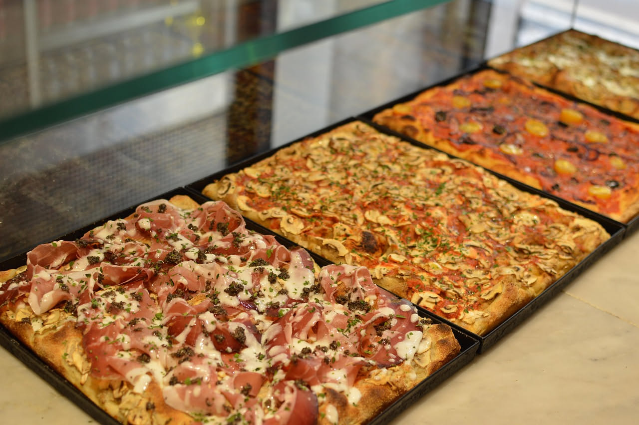 Due fette di pizza a confronto: una romana più sottile e croccante con bordi dorati, una napoletana più alta e soffice con cornicione gonfio